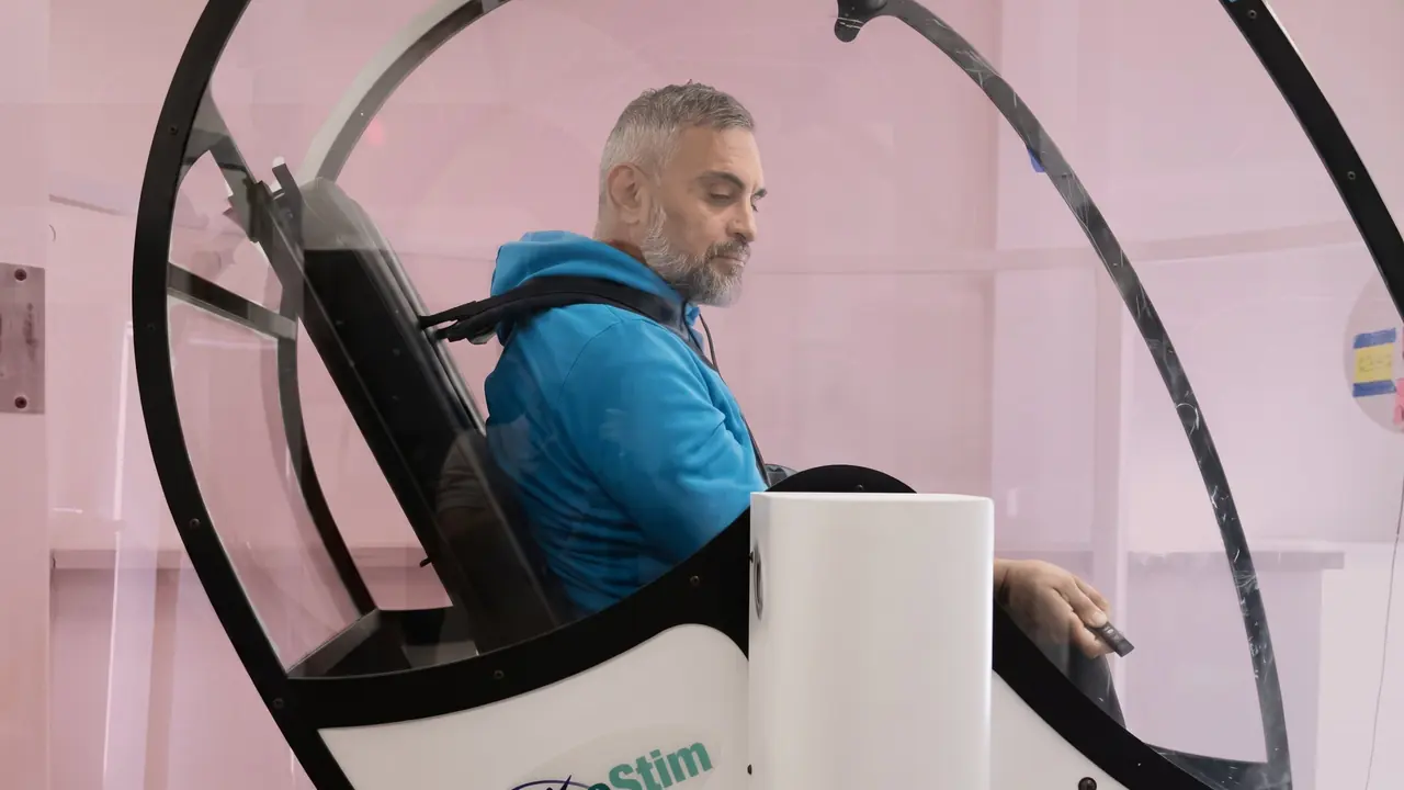 Man in a blue jacket seated in the GyroStim chair holding a laser pointer