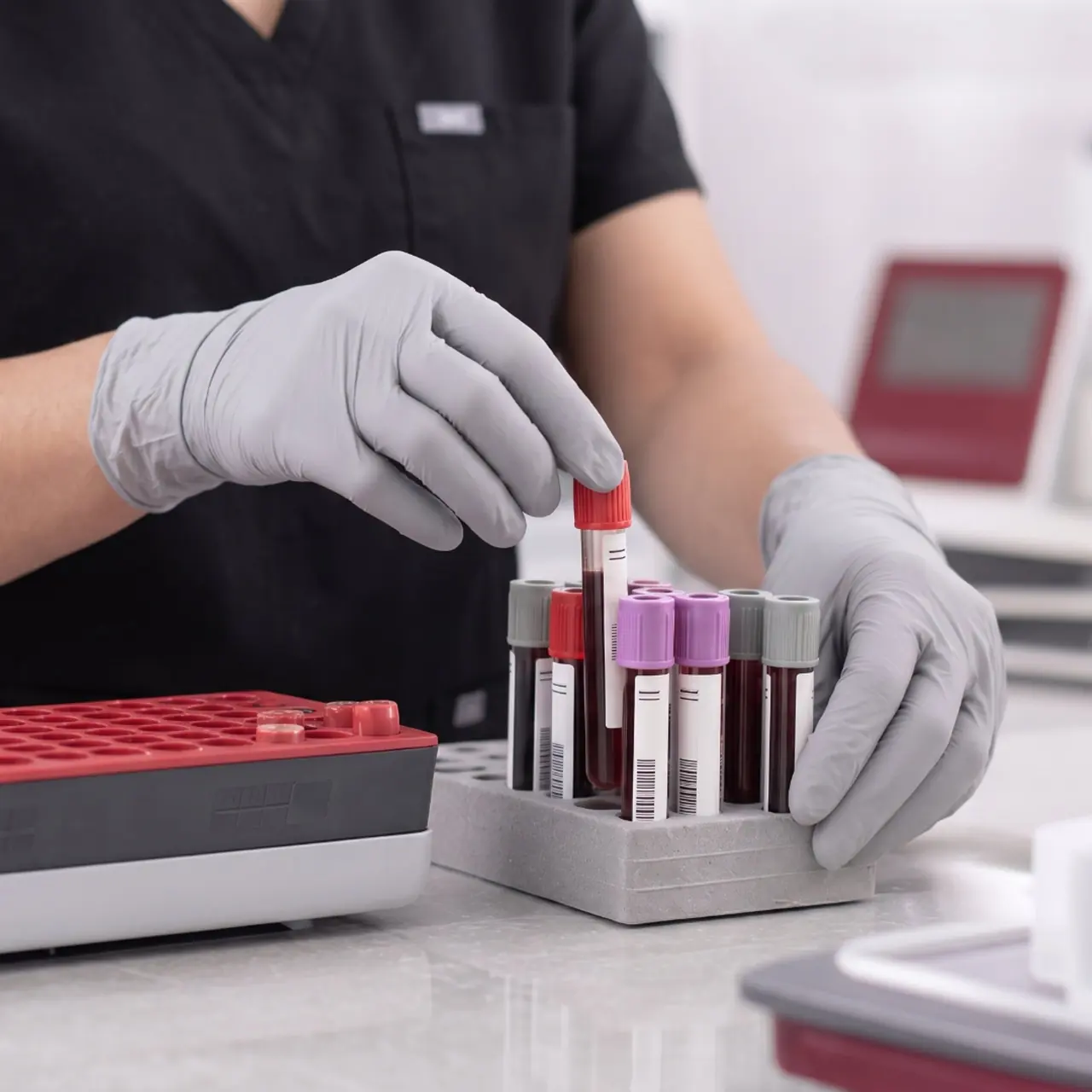 Lab sample handling Gloved hands placing a blood sample tube into a rack of test tubes