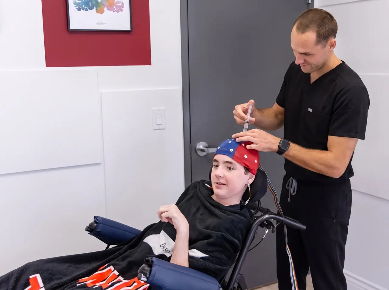 Neurofeedback session Clinician fitting a red and blue EEG cap on a seated young patient