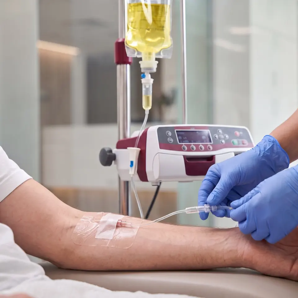 Infusion setup Gloved hands adjusting an IV line beside an infusion pump