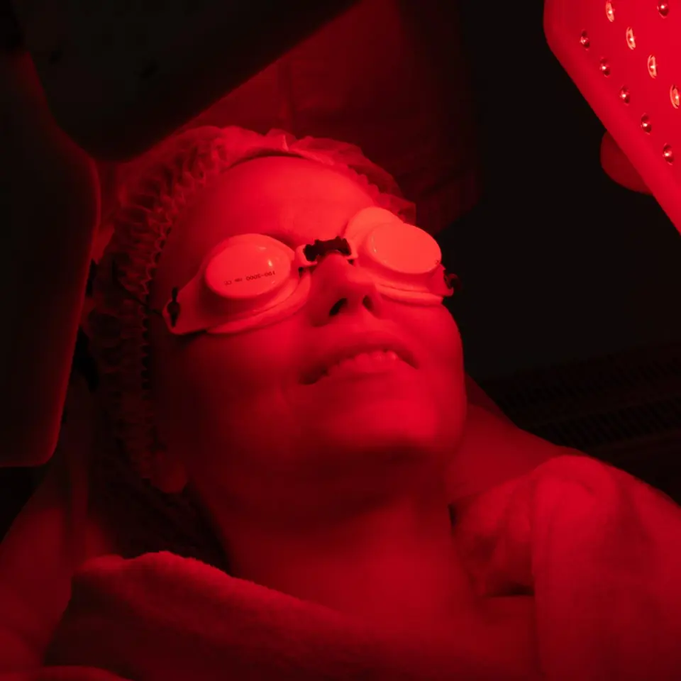 Patient in protective goggles lit by the red glow of a light panel