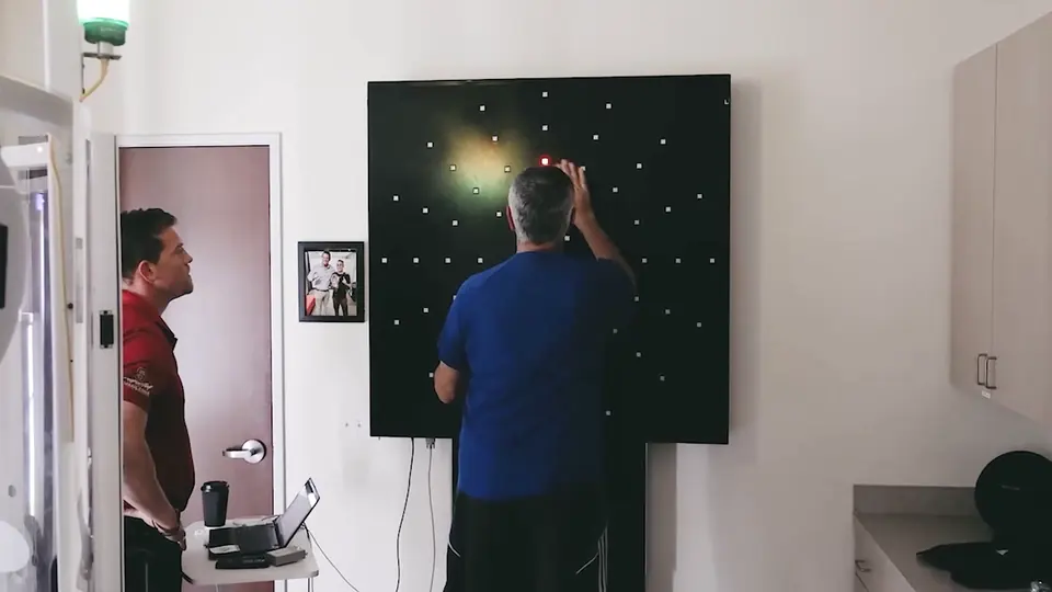 Reaction training Patient reaching for a lit target on a wall-mounted light board as a clinician watches